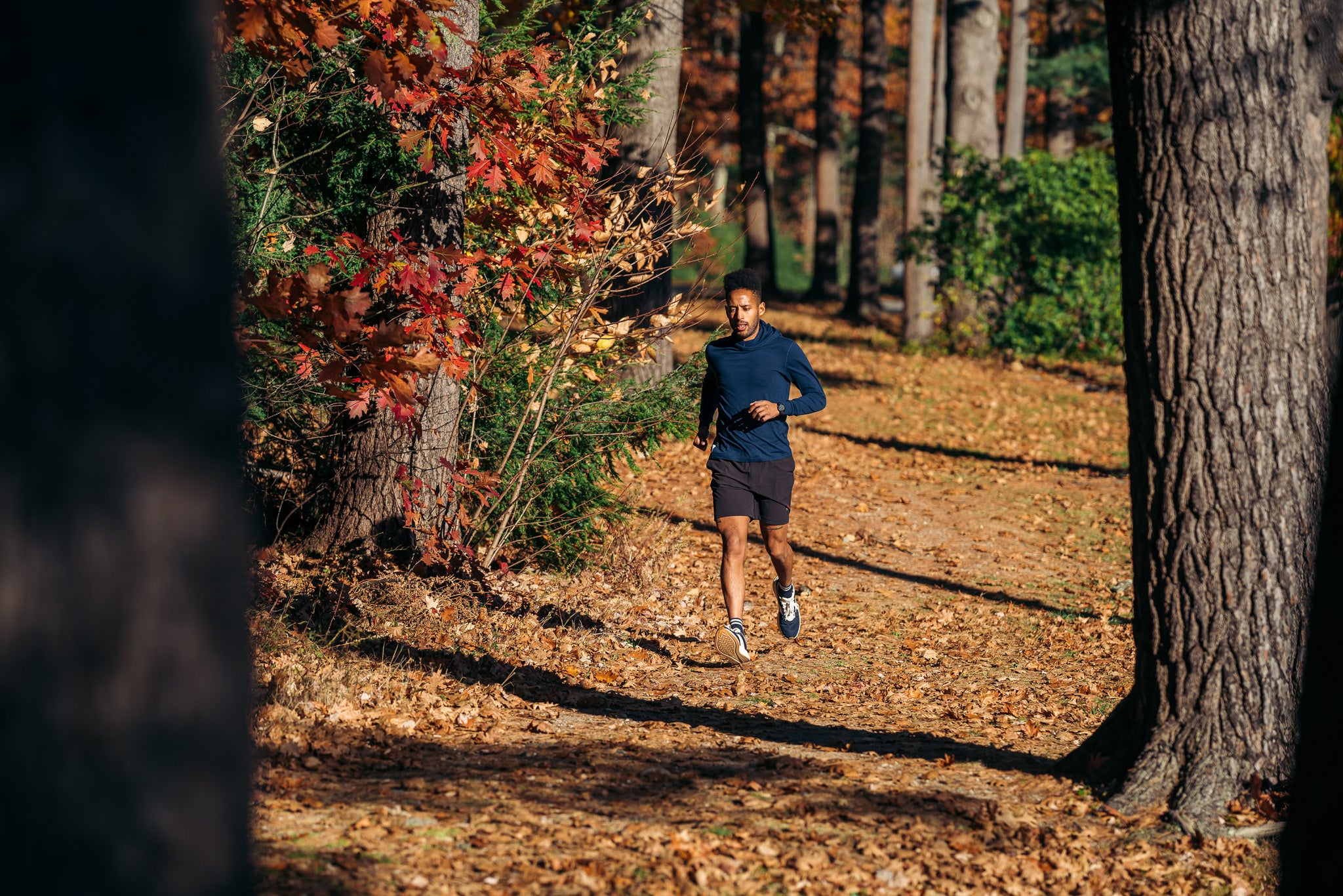 Man running through a natural setting on a dirt path with fall foliage in the background.
