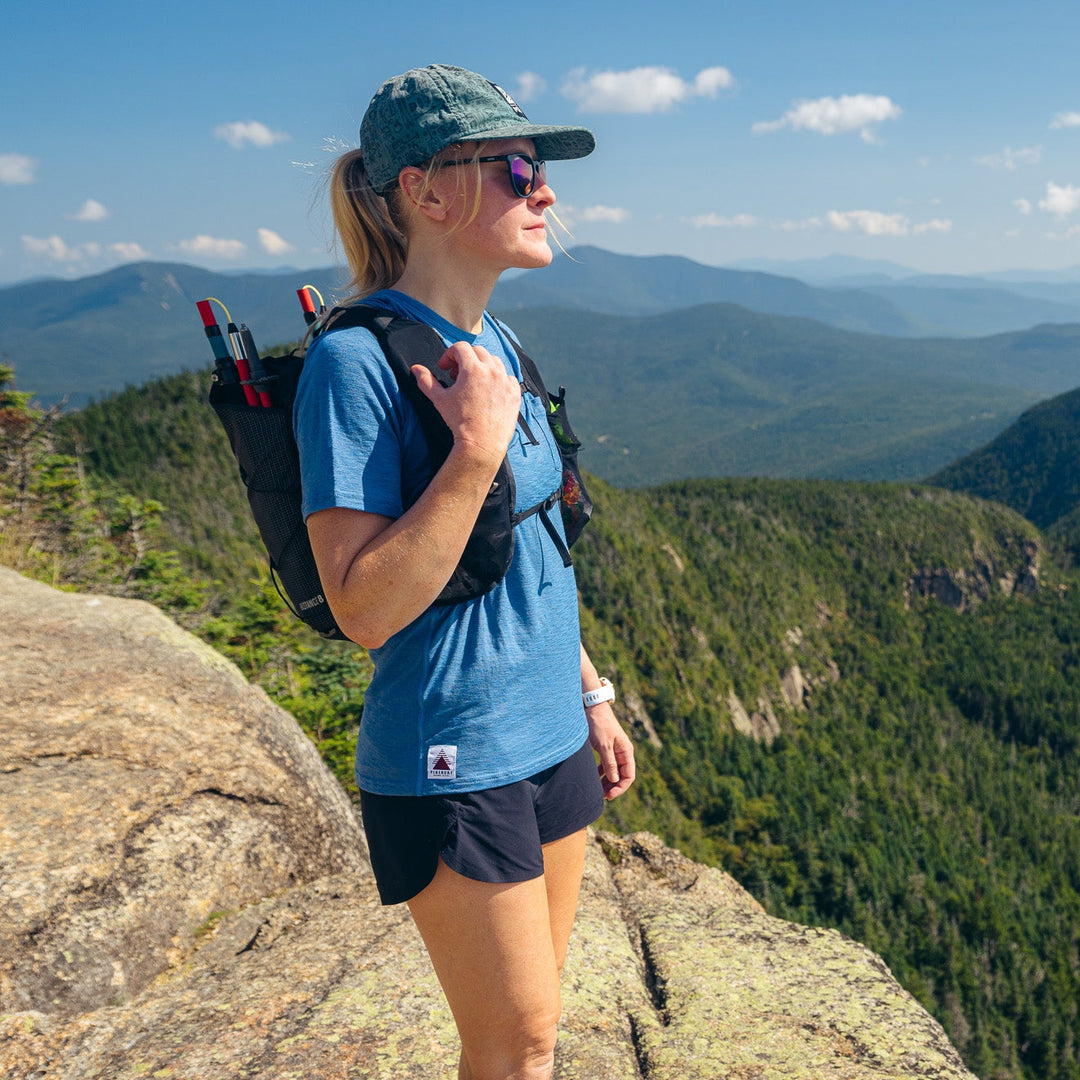 Woman with a backpack standing on a mountain peak overlooking a scenic landscape.
