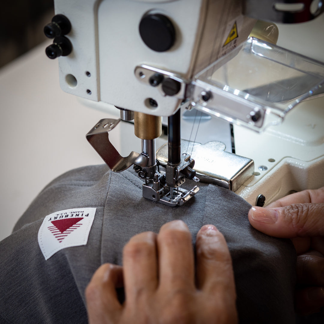 A close up shot of a bottom hem being stitched onto a Pinebury Merino Wool Cycling Jersey in Granite
