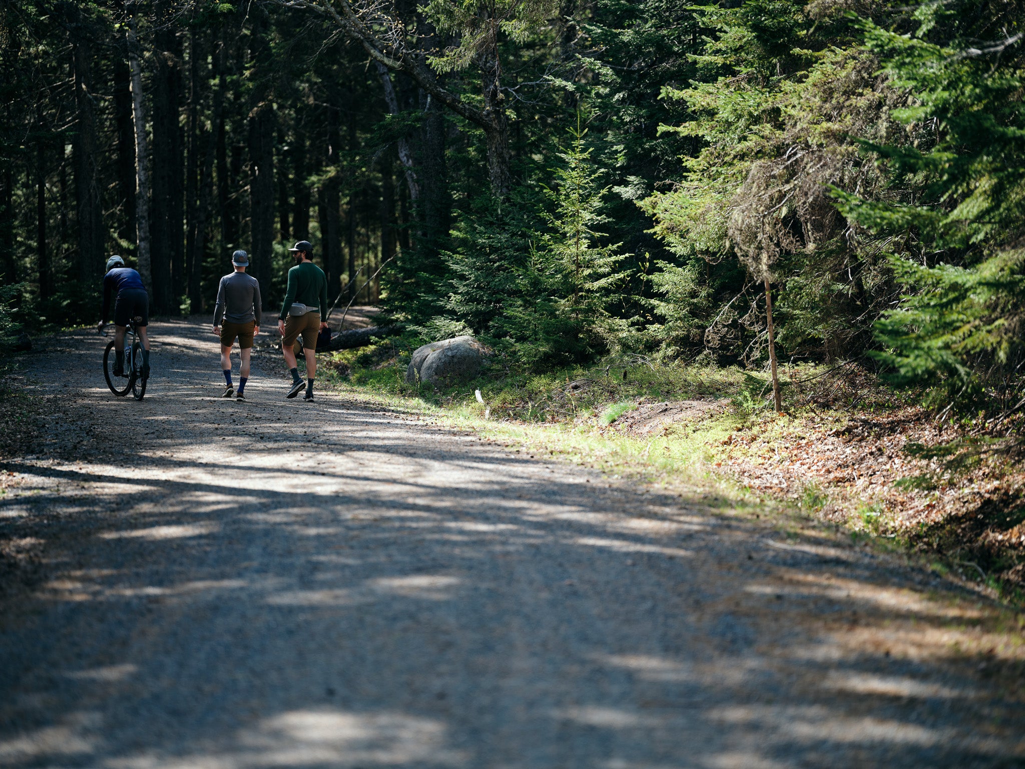 two men walking down a dirt road and one man riding a bike