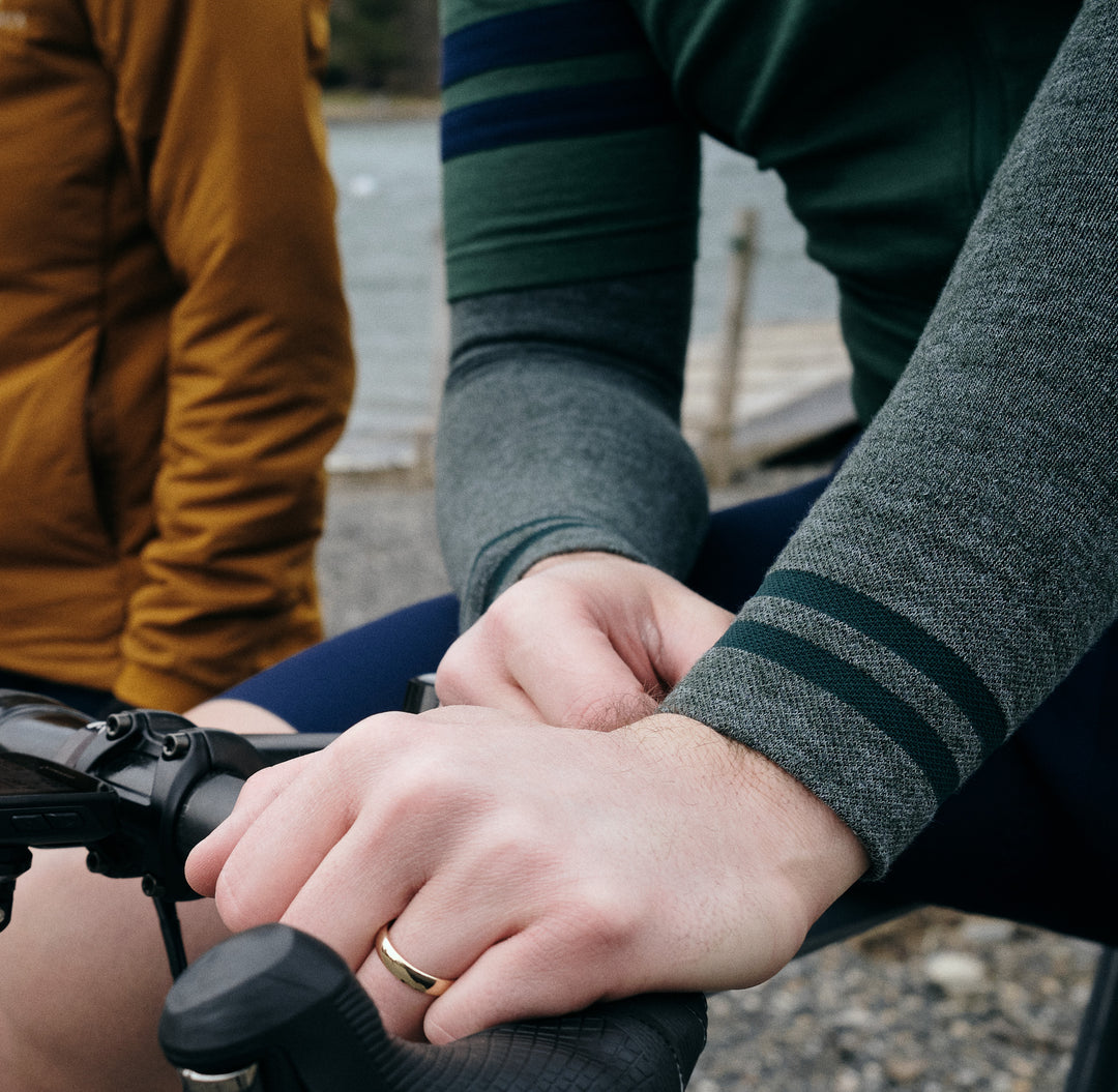 Pinebury Signature Merino Wool Arm Warmers in Loden. Close up detail of cyclists hand on the top of their handlebar showing the stitching of their green arm warmer with two stripes on the wrist.