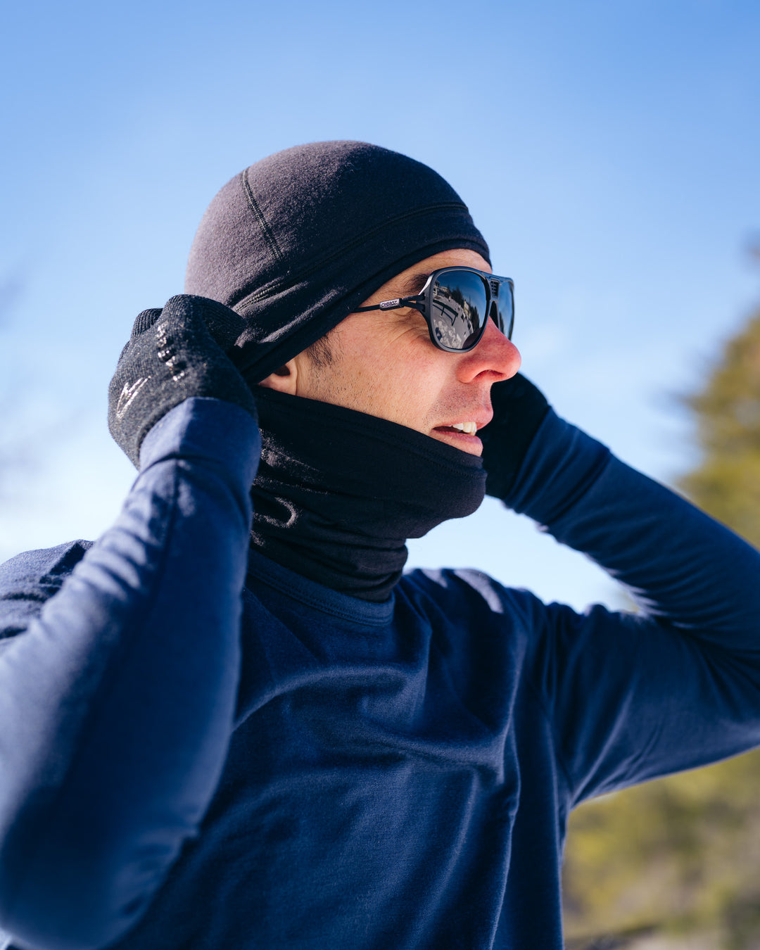 Person wearing a black beanie, sunglasses, and gloves against a blue sky.