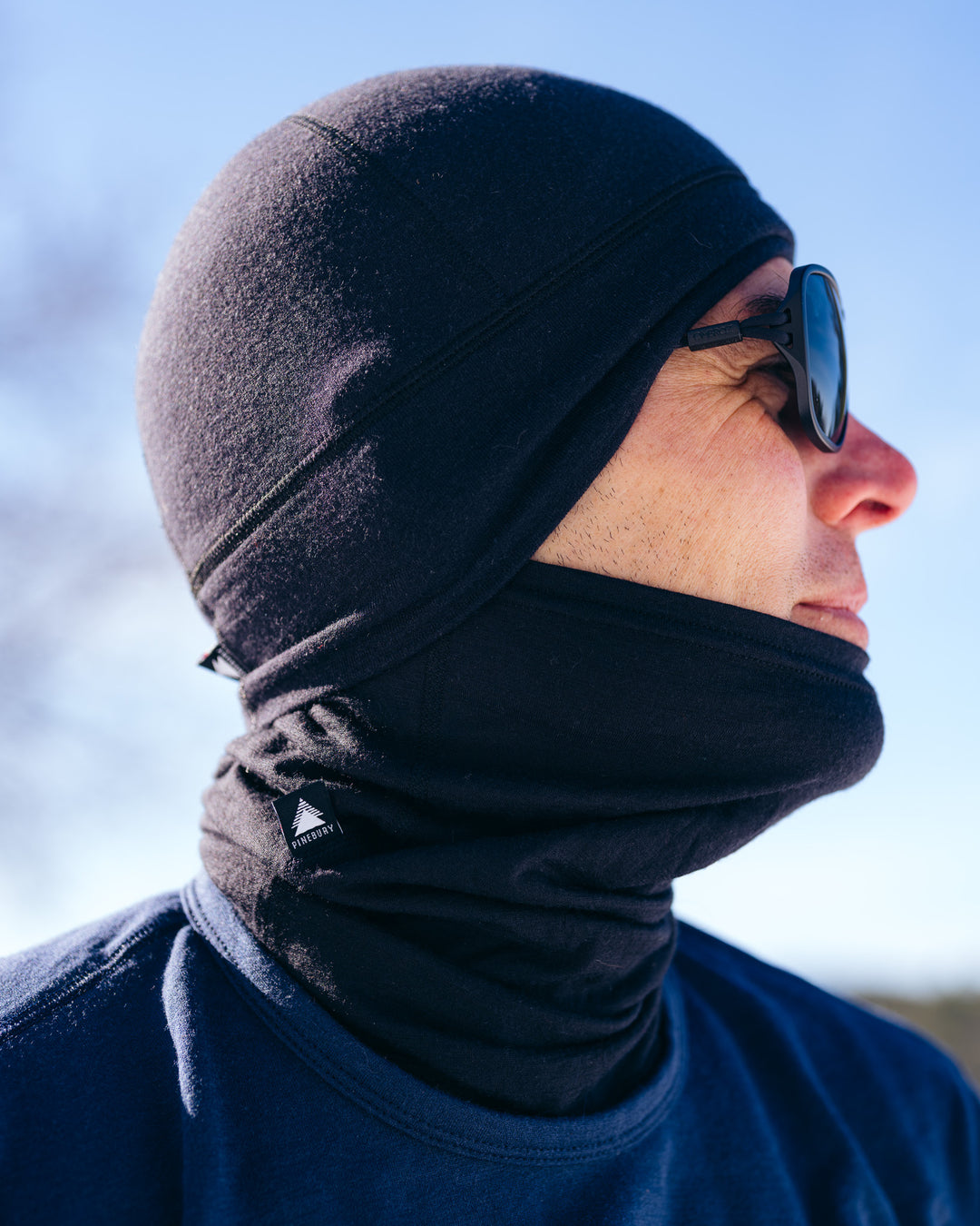 Person wearing a black hat and neck gaiter and sunglasses with a blurred background