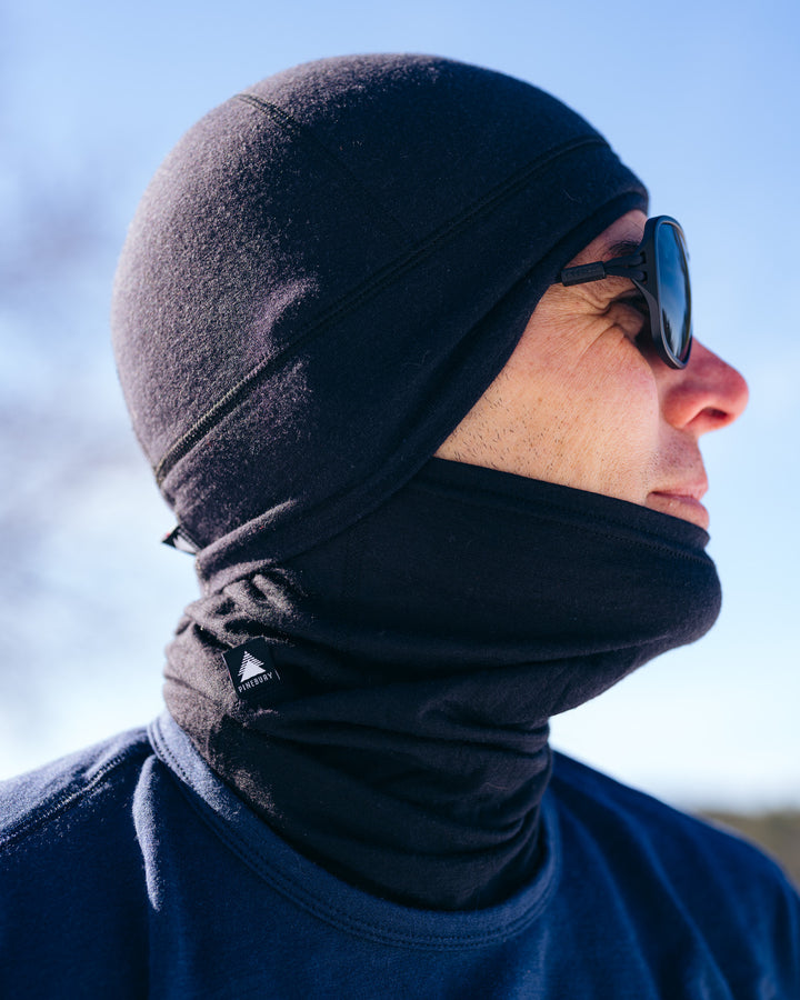 Person wearing a black hat and neck gaiter and sunglasses with a blurred background