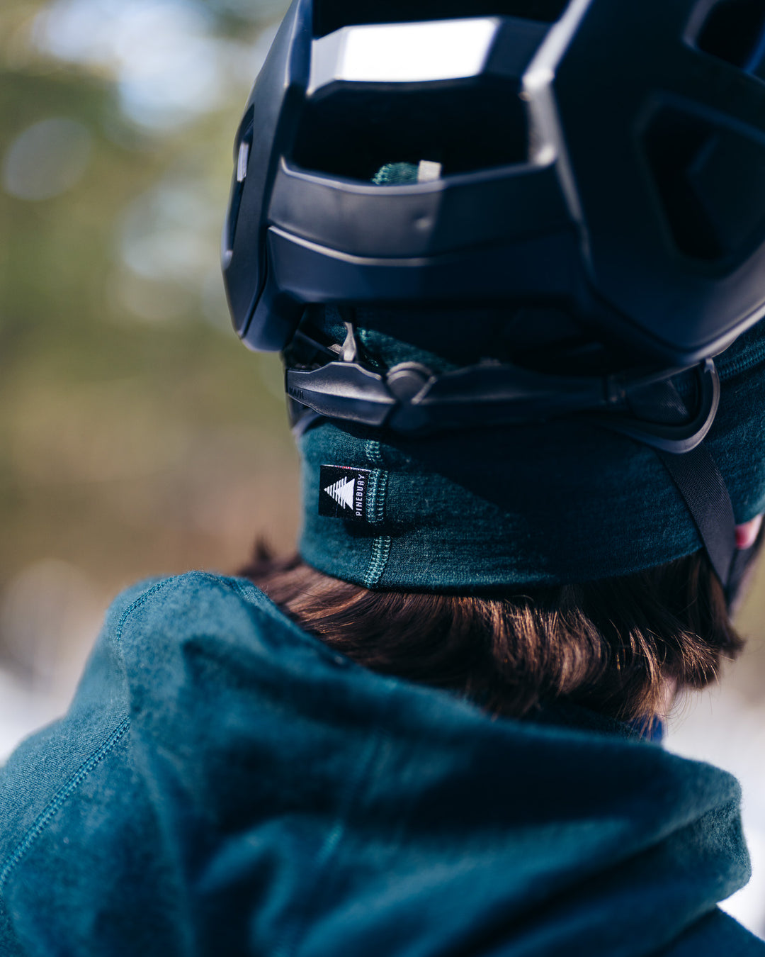 Person wearing a dark helmet and teal beanie with a blurred natural background
