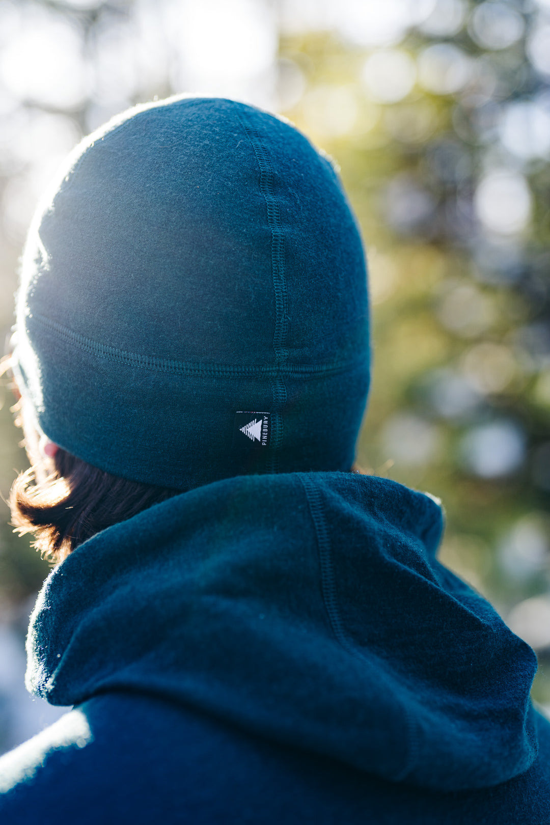 Person wearing a green beanie with a logo, blurred natural background