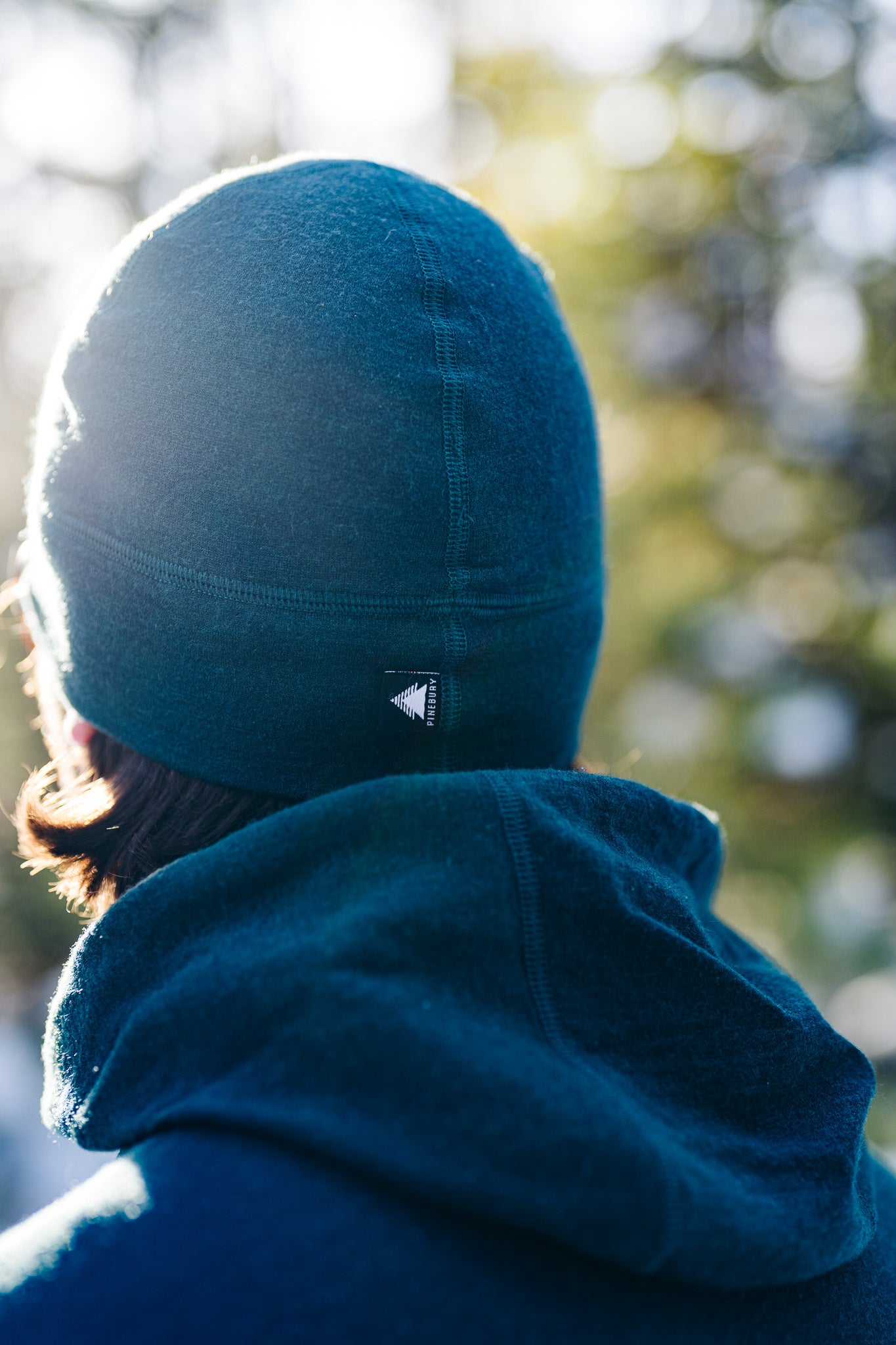 Person wearing a green beanie with a logo, blurred natural background