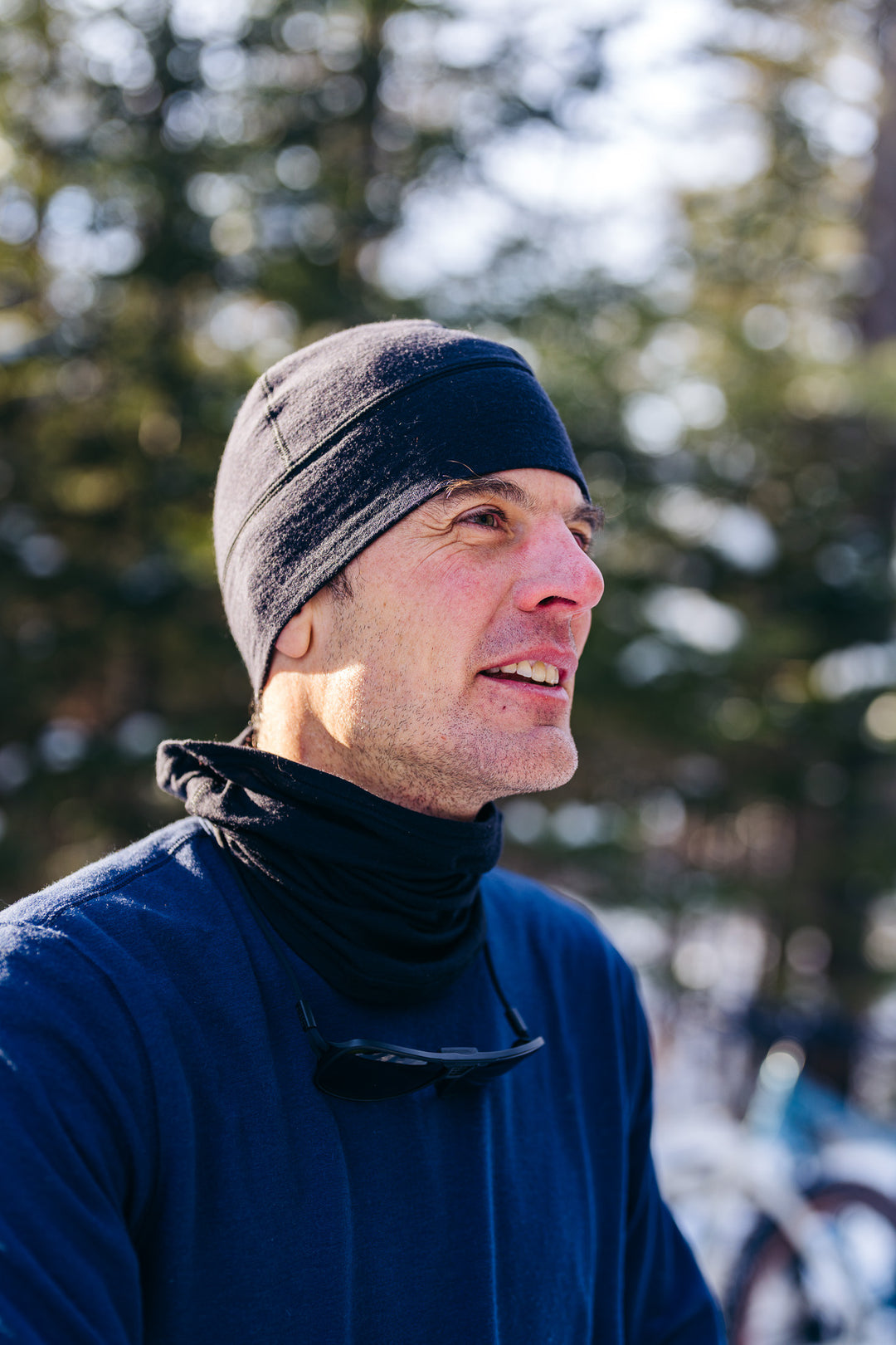 Man wearing a blue shirt and black hat outdoors with trees in the background