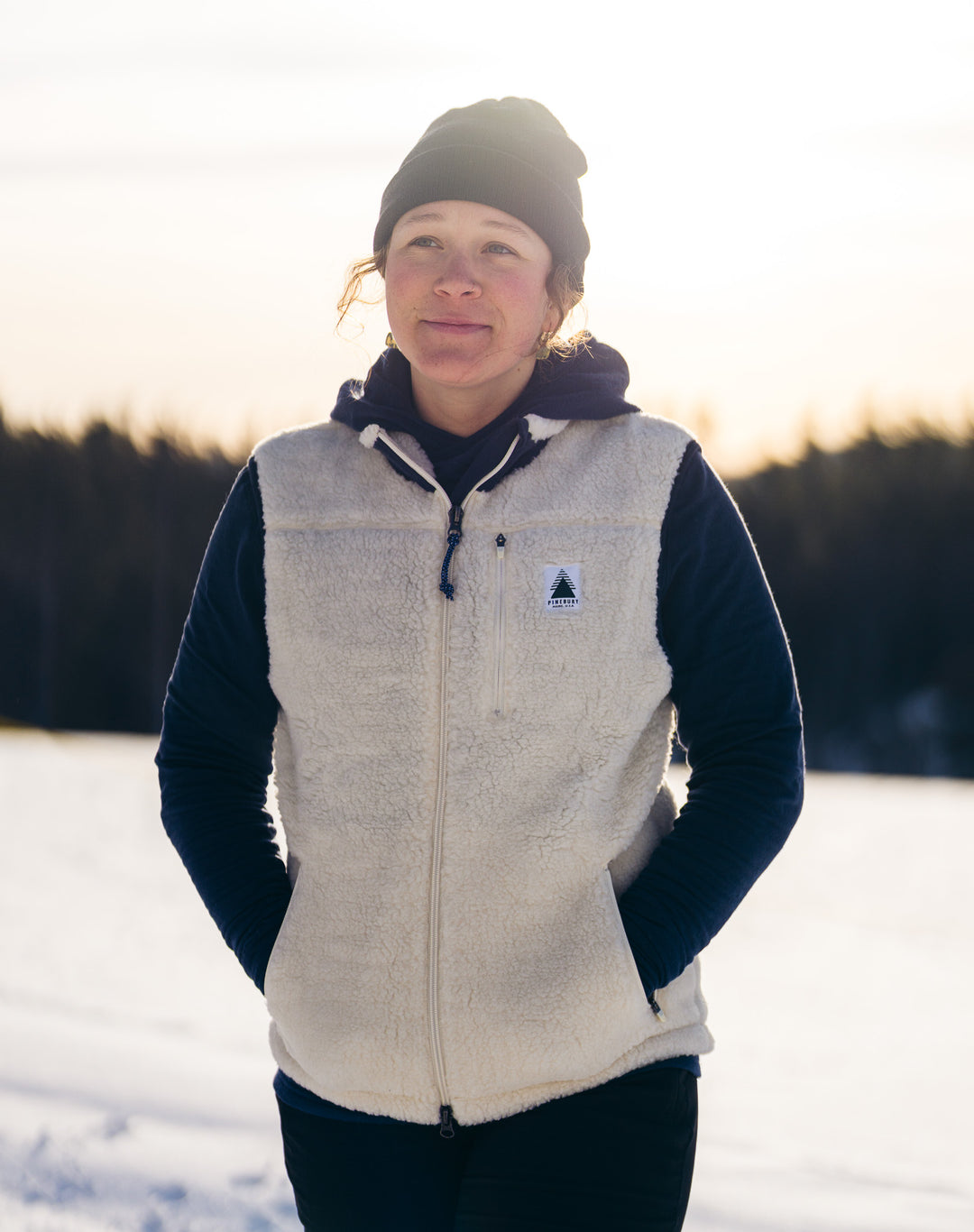 Person wearing a white fleece vest with a logo in a snowy landscape