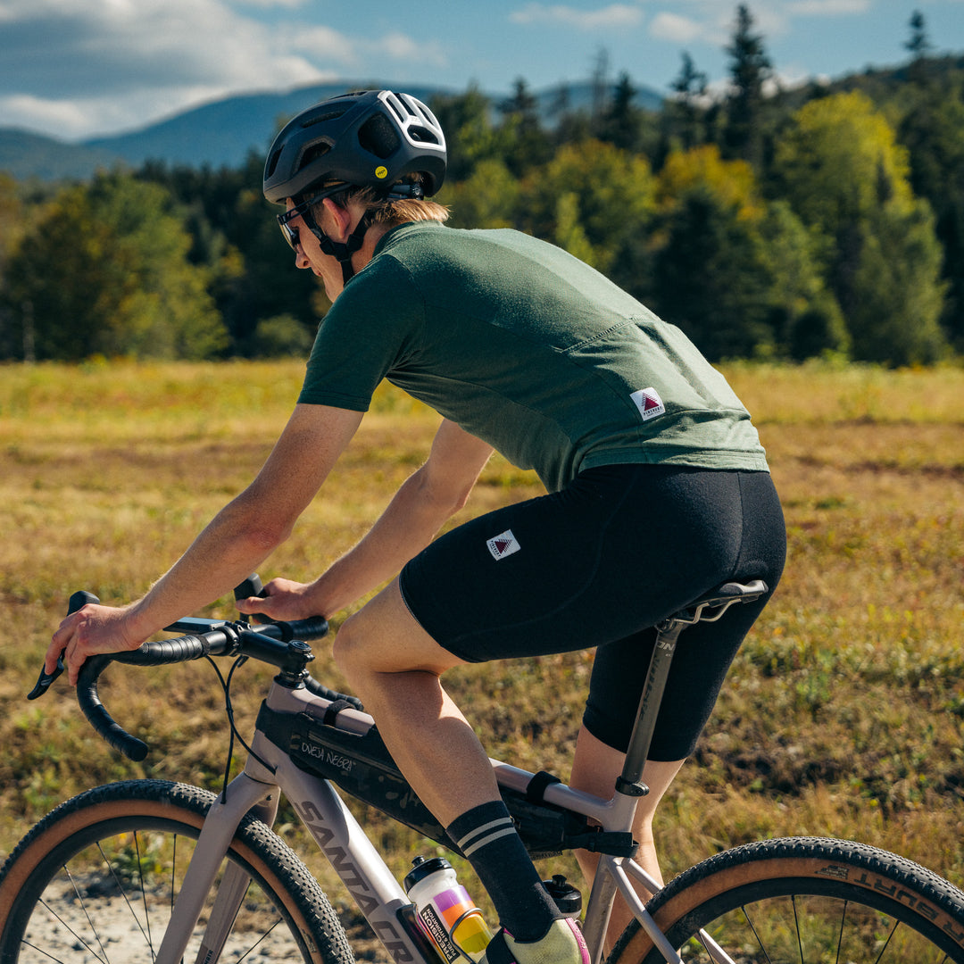 Person riding a bicycle in a natural setting with trees and mountains in the background