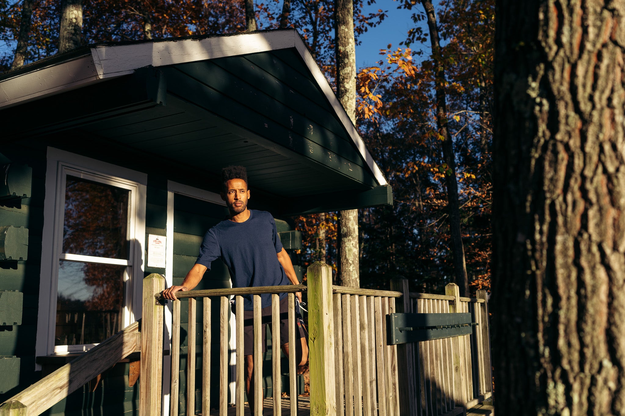 Man standing on a wooden deck of a cabin with trees in the background
