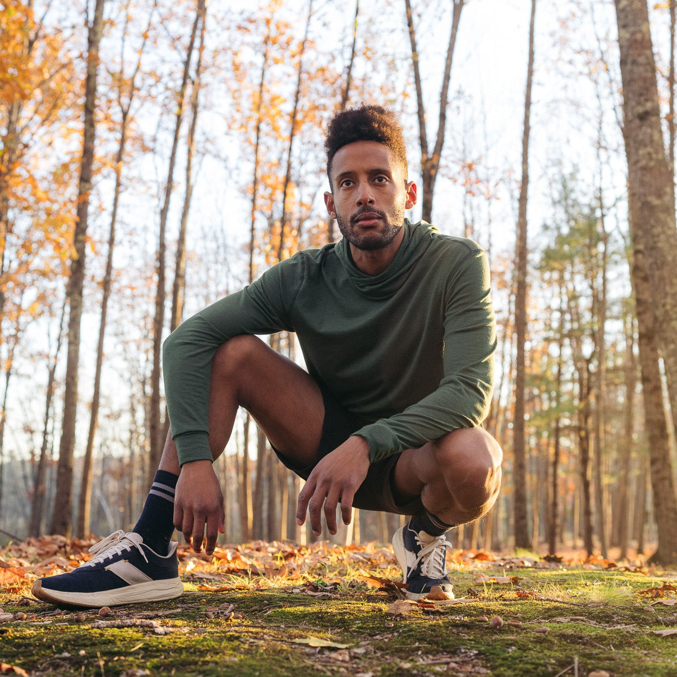 Man in athletic wear squatting in a forest with autumn leaves