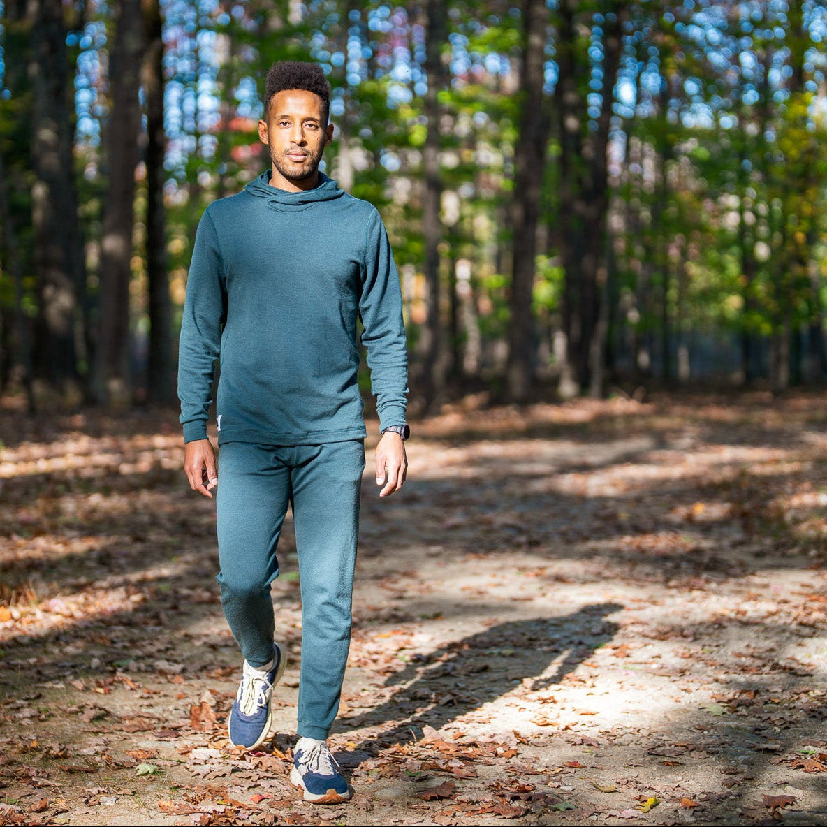 Person walking on a path in a forest wearing a green tracksuit.