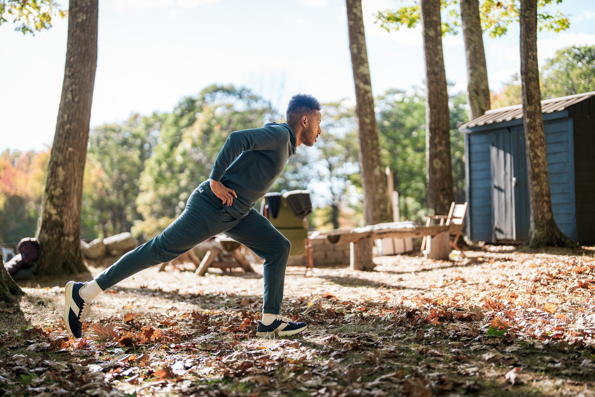 Man stretching outdoors in a forested area with trees and a shed in the background.