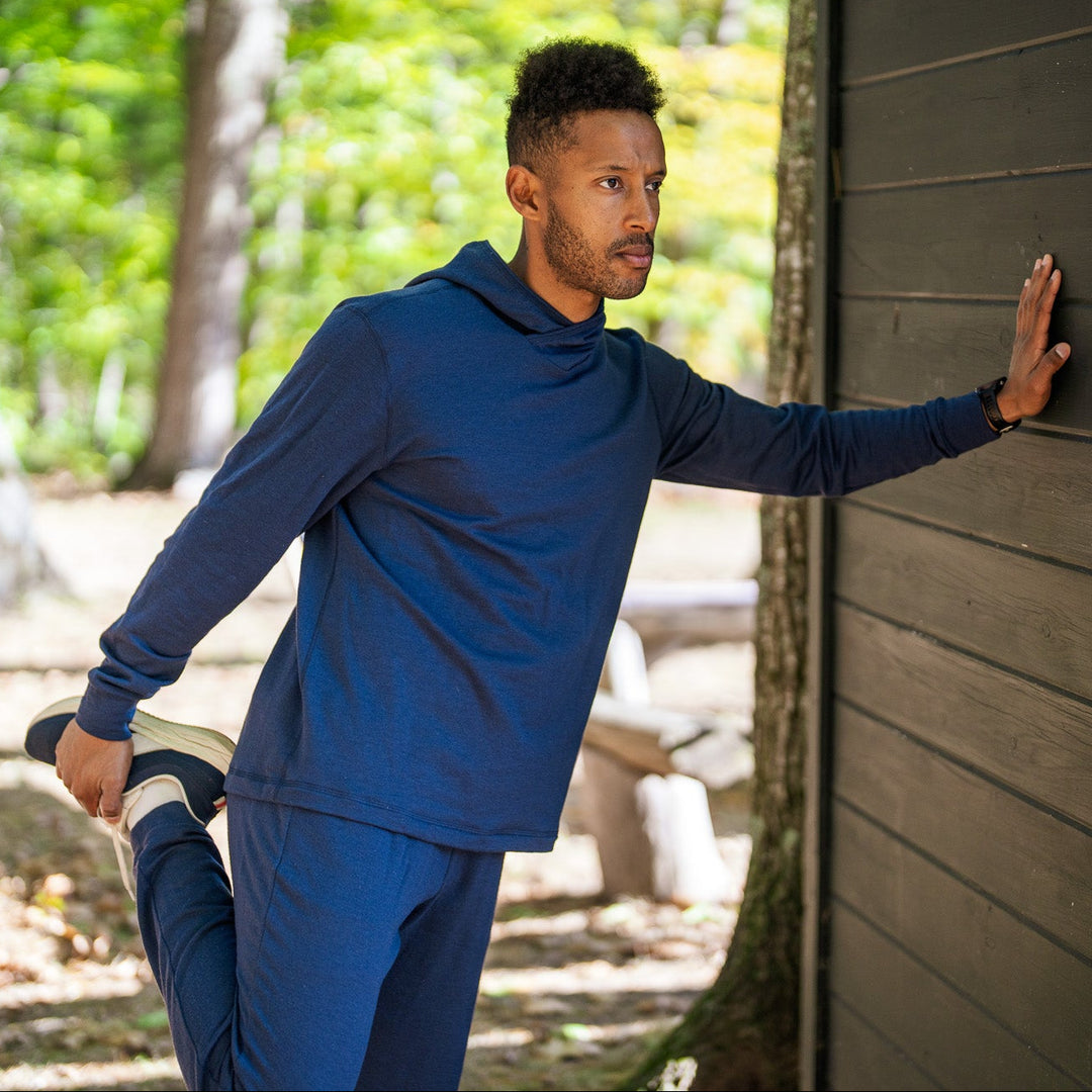 Man in blue athletic wear stretching outdoors near a wooden building.