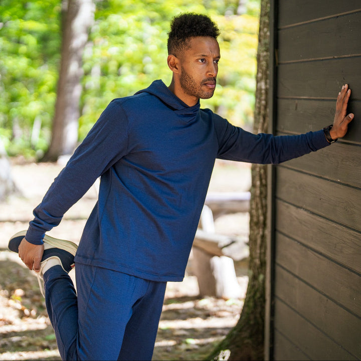 Man in blue athletic wear stretching outdoors near a wooden building.