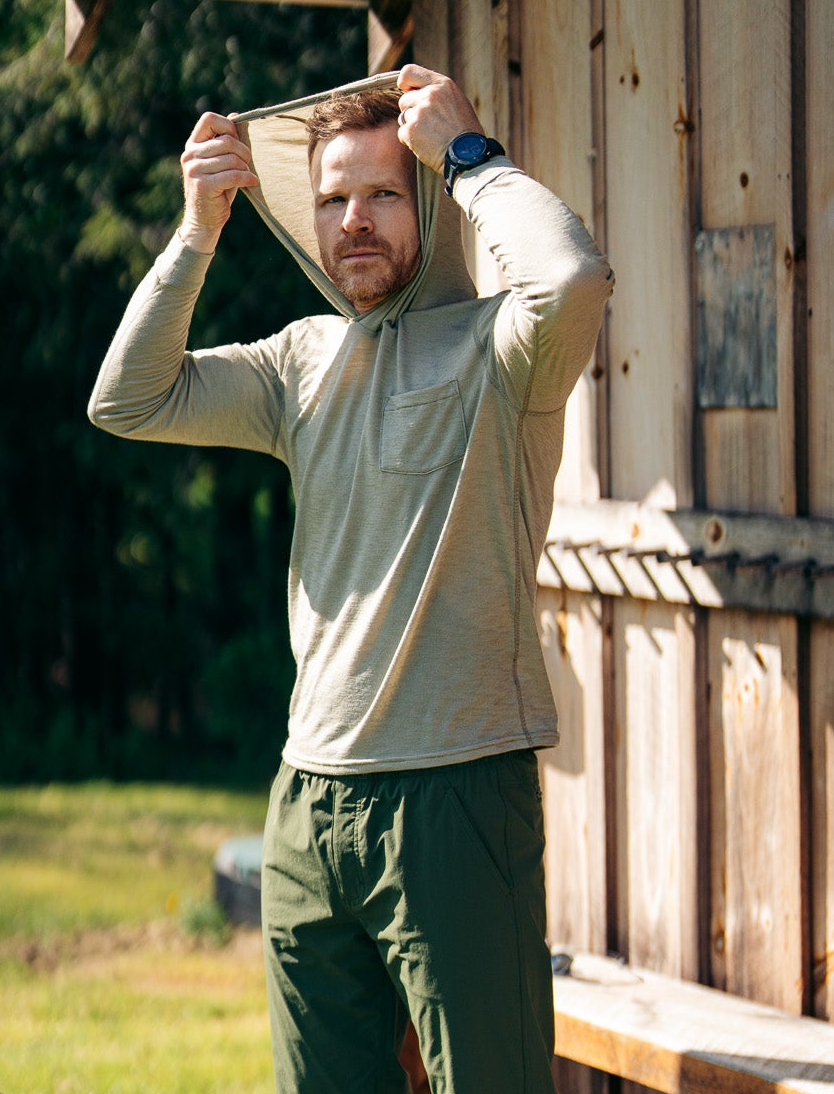 Man adjusting a hoodie outdoors near a wooden cabin and bicycle