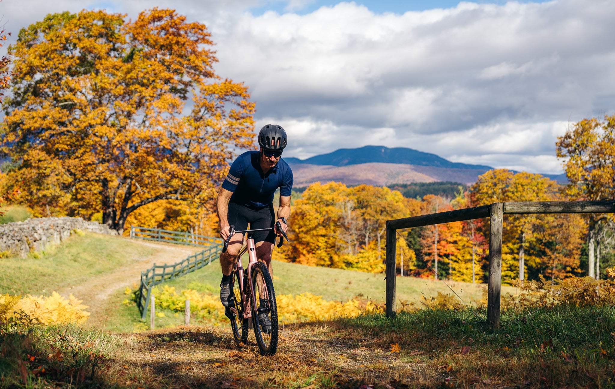 Person riding a bicycle on a trail with autumn foliage and mountains in the background