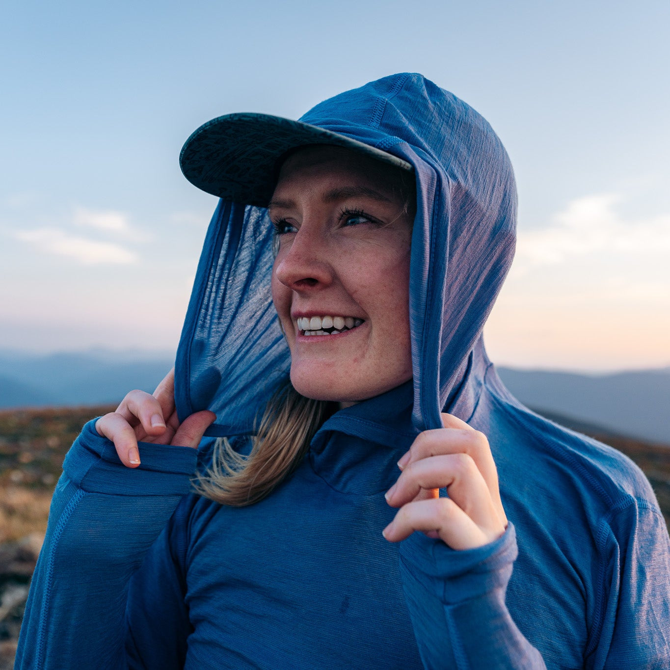 Person wearing a blue hooded jacket on a mountain at sunset