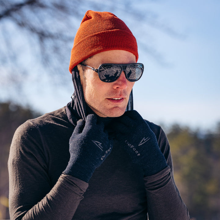 Person wearing a red beanie, sunglasses, and gloves in a snowy landscape