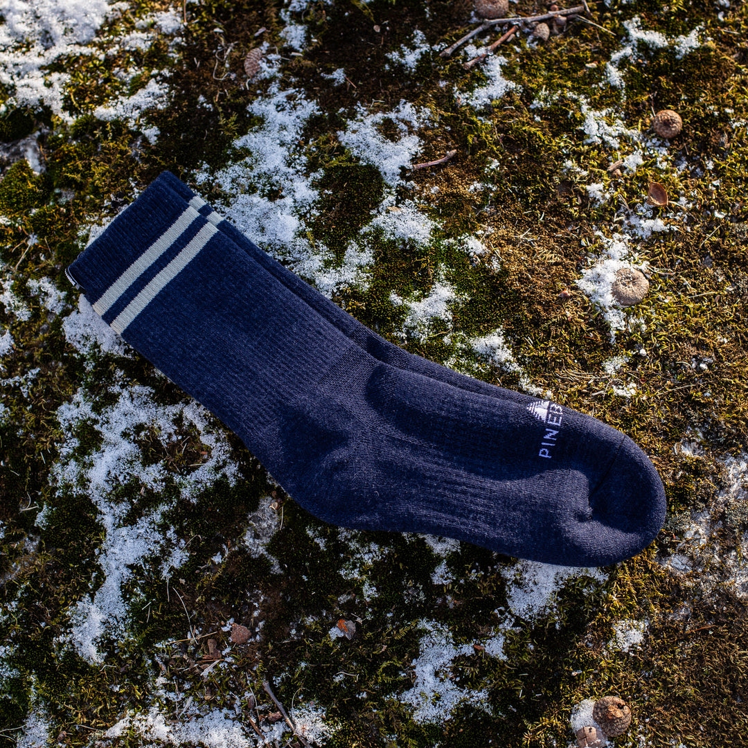 Blue sock with white stripes on a mossy ground with patches of snow