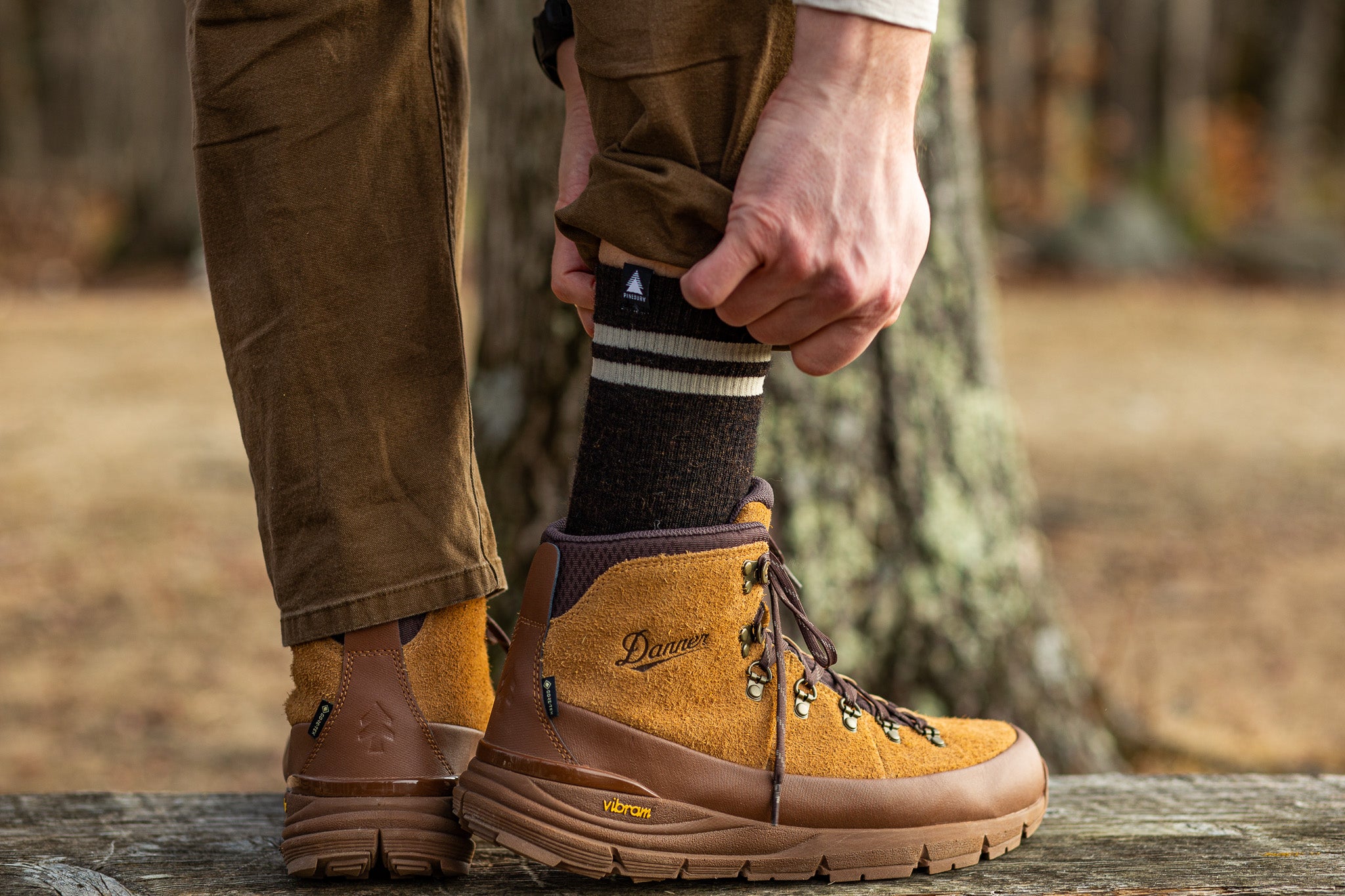 Person wearing brown hiking boots with visible brand logo, standing outdoors.
