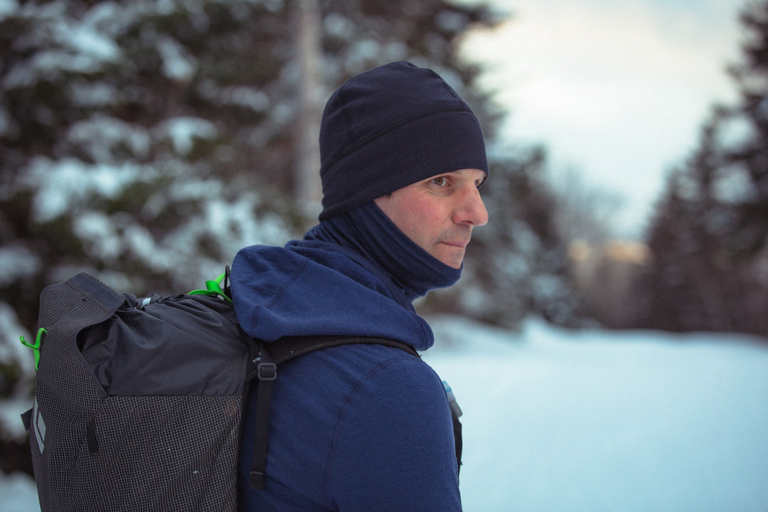 person wearing a black beanie and blue sweatshirt in a snowy forest