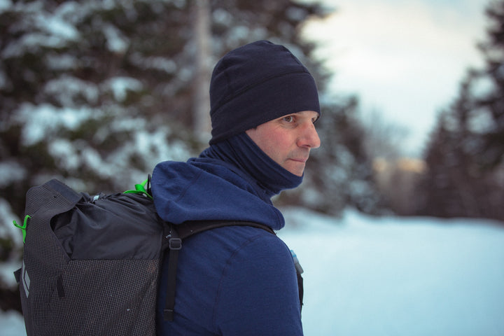 person wearing a black beanie and blue sweatshirt in a snowy forest