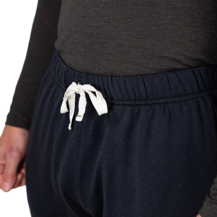 Person wearing dark blue sweatpants with a white drawstring on a plain background