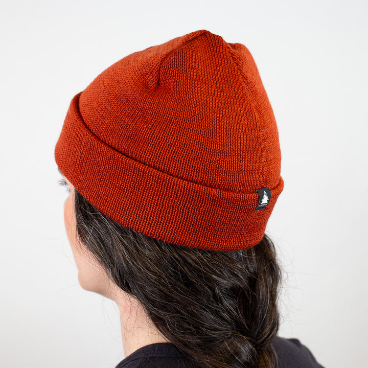 Person wearing an orange knit beanie with a logo on a white background