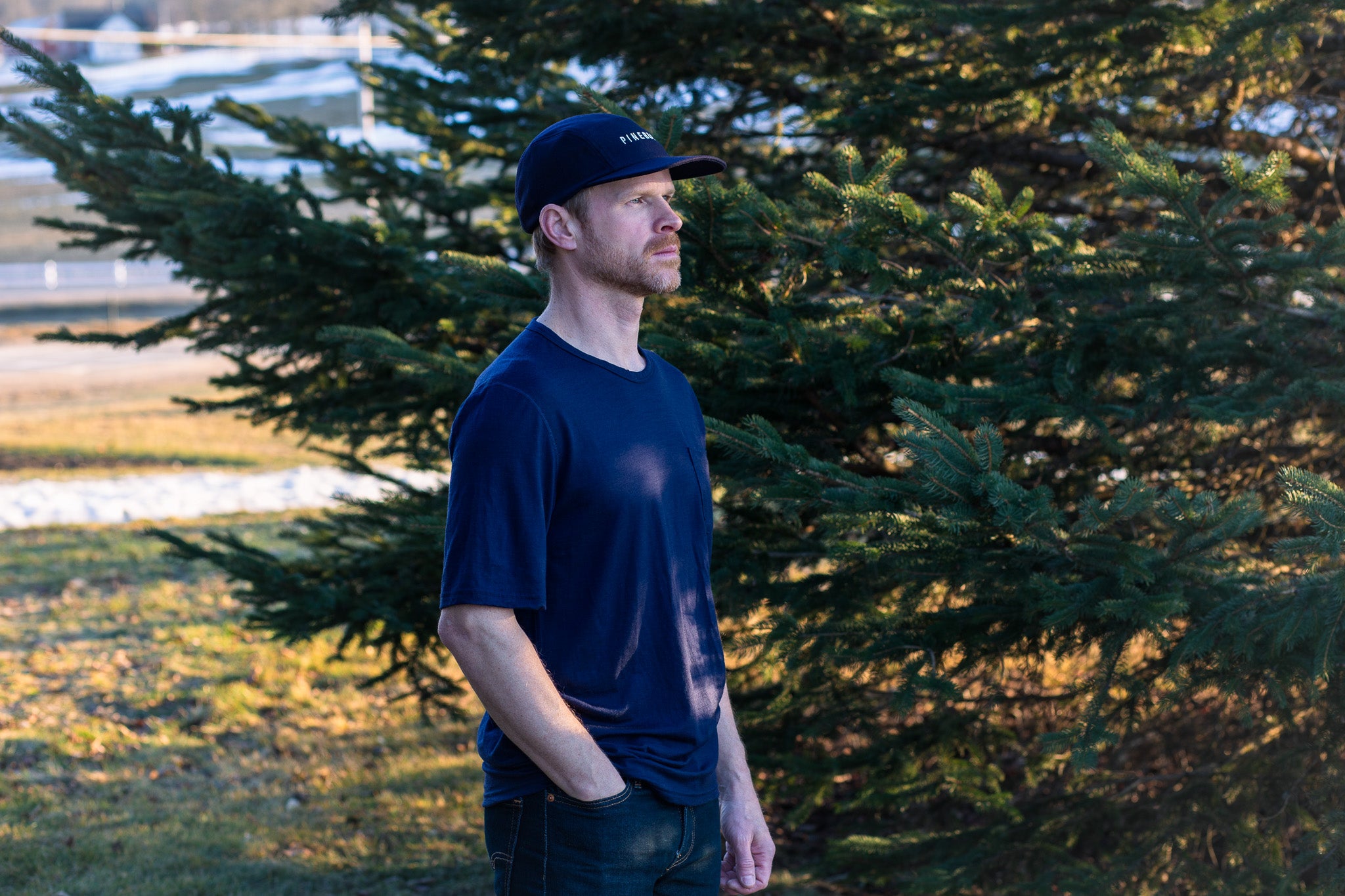 Man wearing a navy blue t-shirt and cap standing in front of trees