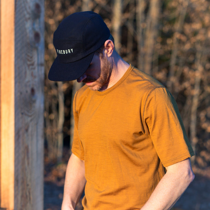 Man wearing a mustard yellow t-shirt and navy cap with &