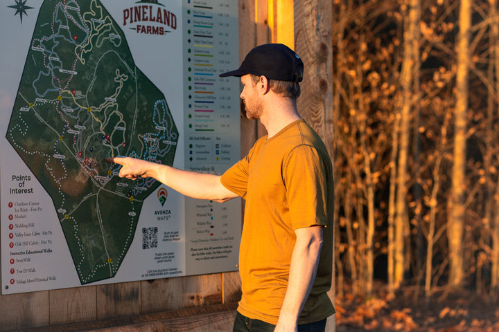Man pointing at a map of Pineland Farms in a forest setting