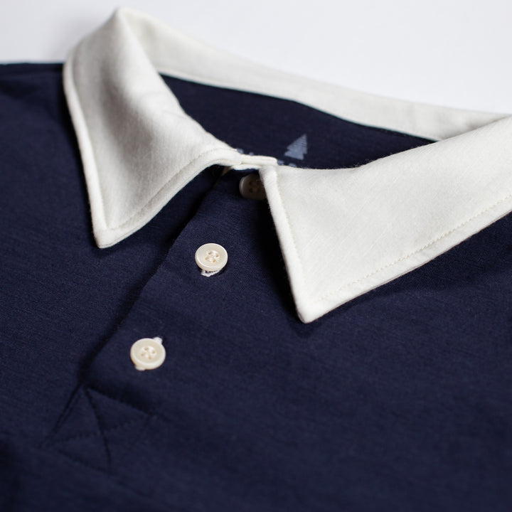 Close-up of a polo shirt collar in off-white contrasting with a dark navy body, featuring two white buttons.