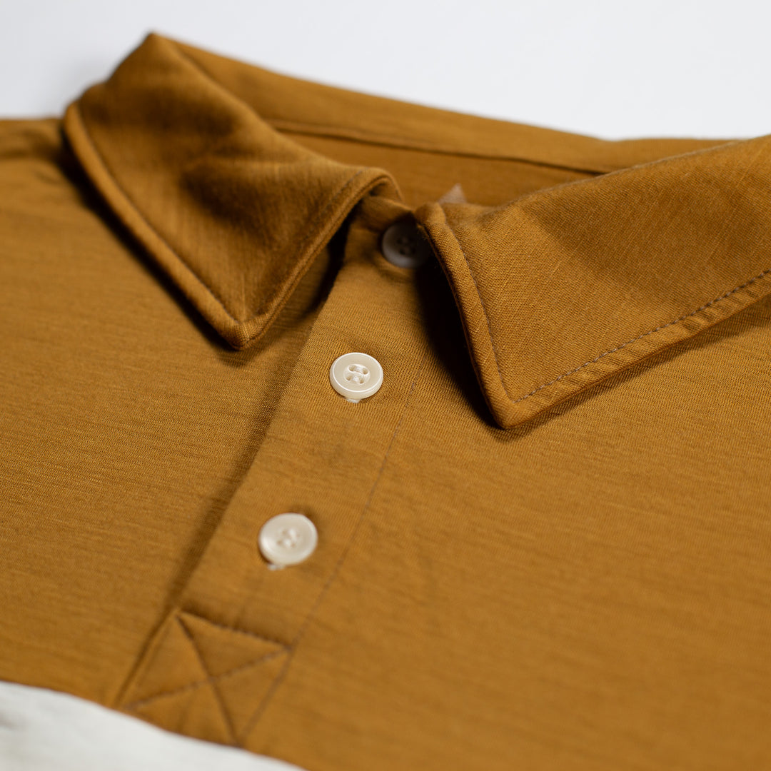 Close-up of a mustard yellow or ochre-colored polo shirt collar with two white buttons, showing the fabric texture and stitching details.