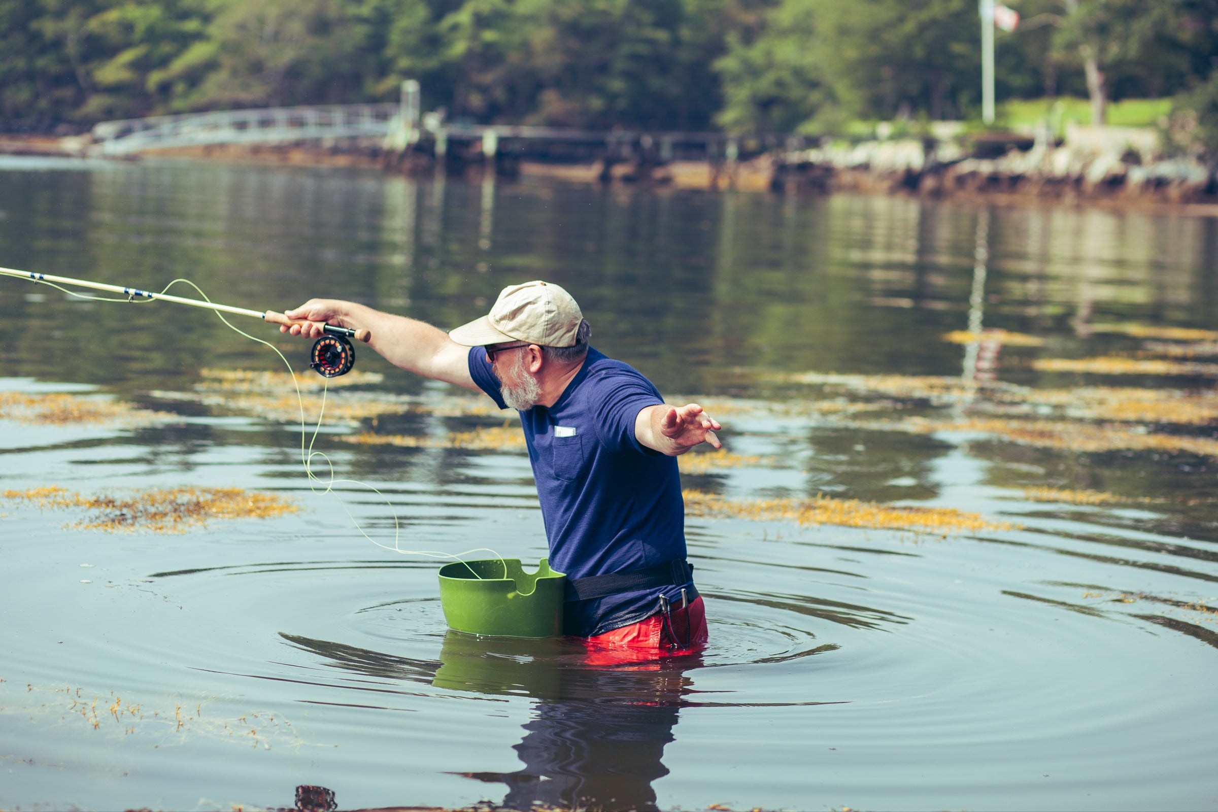 Man fishing in a bay with trees and a dock in the background