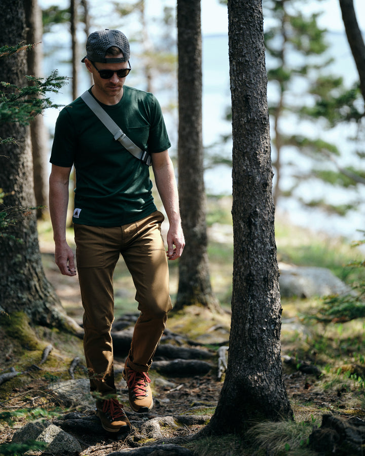 Pinebury Portland Short Sleeve Merino Wool Performance Tee in Pine, Man walking casually on a sunny trial in the woods with a sling bag and brown pants