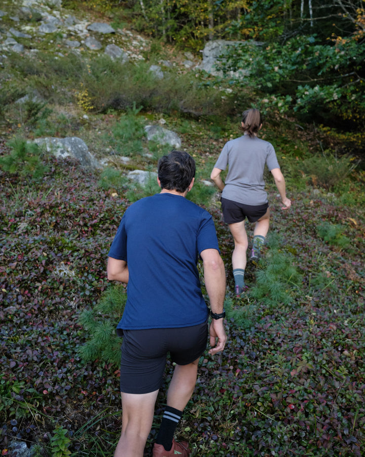 Pinebury Portland Short Sleeve Merino Wool Performance Tee in Atlantic Blue, Man and Woman trail running up a steep trail on rocks in a blueberry field in Maine