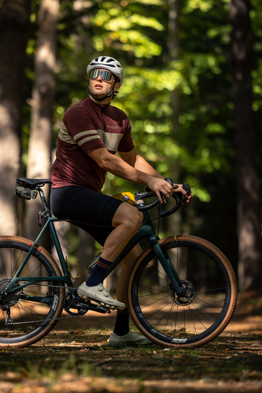 Rider on a gravel bike in the pines wearing the Brick Red Every-Season Quarter Zip Jersey