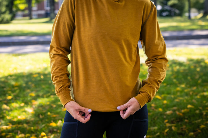 A person outdoors wearing a mustard yellow long-sleeve athletic shirt and black leggings, standing in a grassy park area.