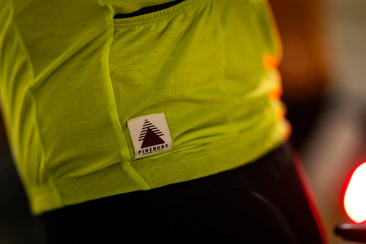 Close-up of a bright lime green athletic top with a white PINEBURY brand patch on the front, worn by a person in low light.