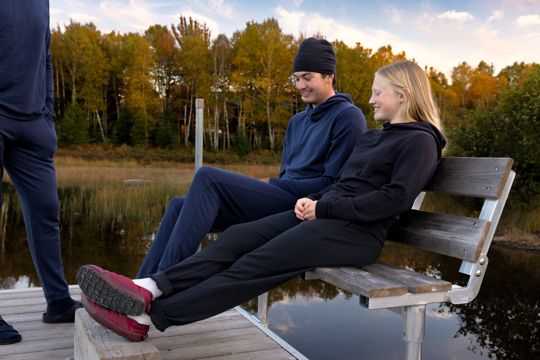 Two people sitting on a wooden bench by a lake with trees in the background