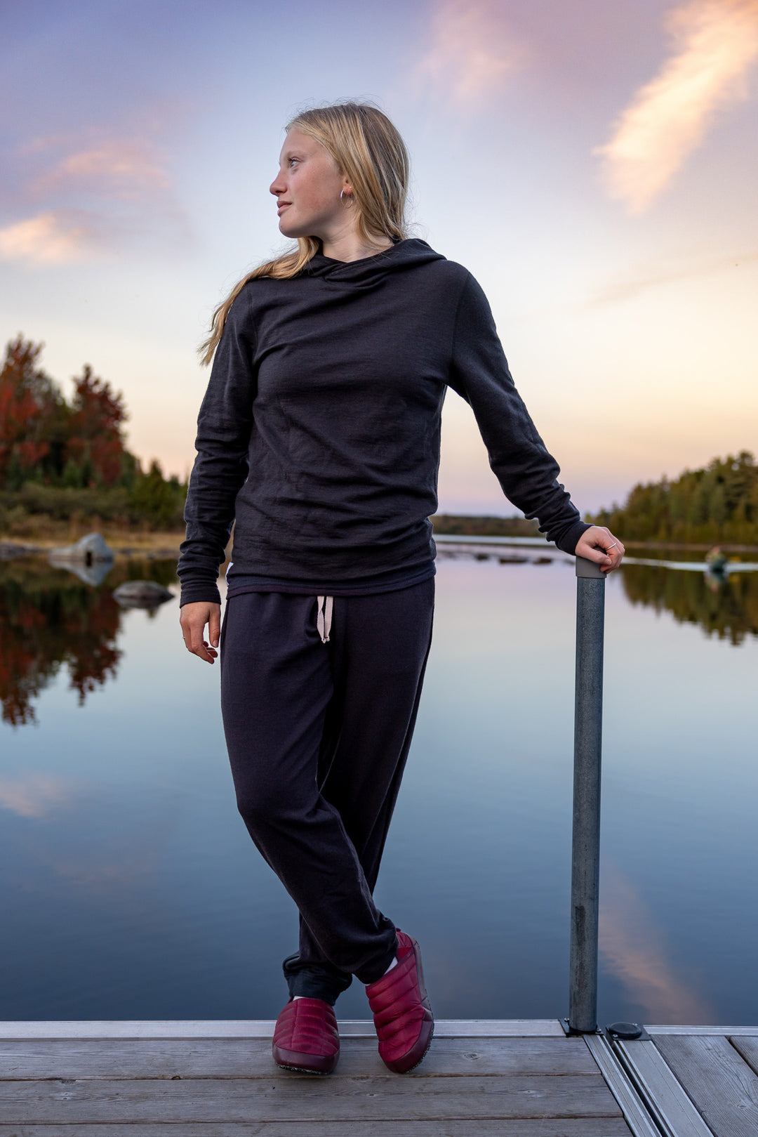 Woman standing on a dock by a lake wearing a dark outfit with pink shoes.