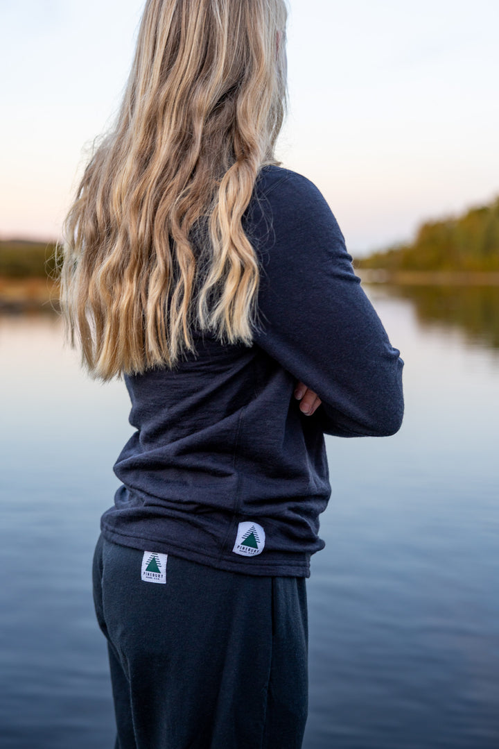 Person wearing a navy long-sleeve shirt and pants with a lake and trees in the background