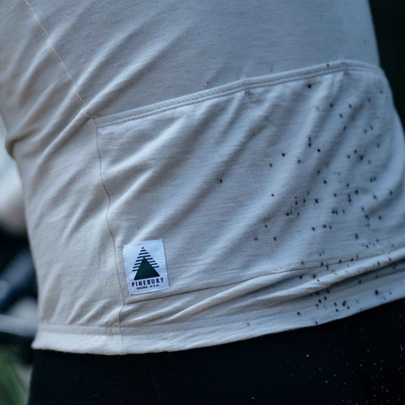 A close up shot of the back pockets on a Pinebury Grafton Long Sleeve Cycling Jersey in Moonbeam, with some dirt spray from the back tire