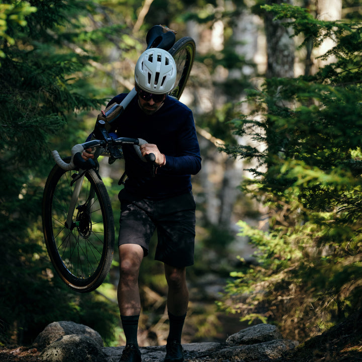 Pinebury Portland Long Sleeve Performance Tee in Atlantic Blue, Man carrying his gravel bike up a rock path in the woods