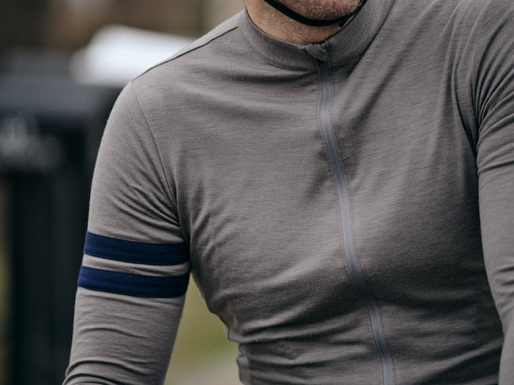 Pinebury Rangeley Long Sleeve Merino Wool Cycling Jersey in Granite. Close up of the detail on a grey wool cycling jersey with two blue stripes on the right bicep and a matching grey zipper.